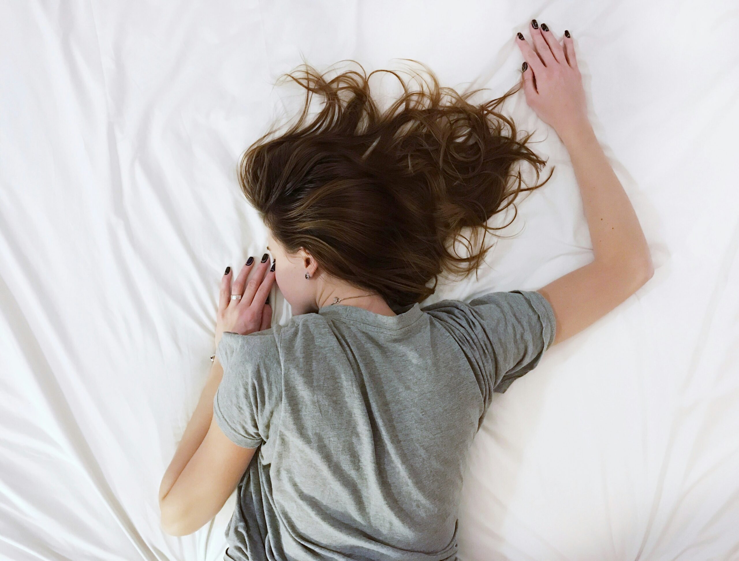 A young woman at rest sprawls facedown on crisp white sheets.